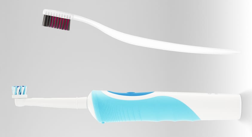 A white and blue electric toothbrush faces a white manual toothbrush with red and navy bristles