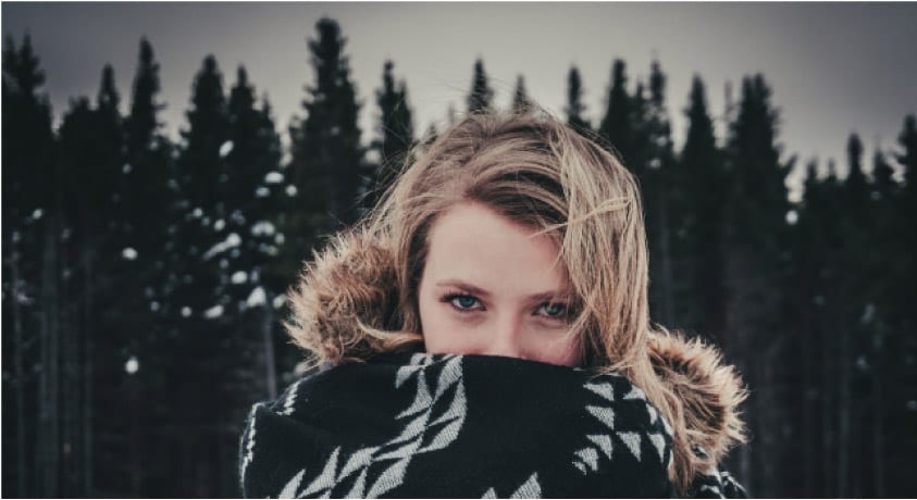 girl wrapped in a blanket covering her mouth with a forest backdrop